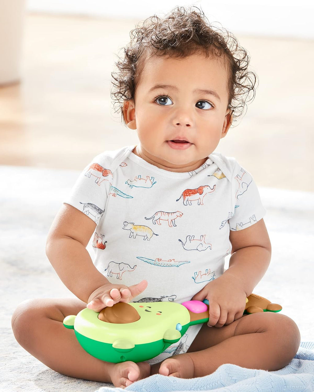 Baby holding green avocado guitar toy while sitting, reaching toward light-up buttons