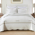 White cotton quilt coverlet with stitched floral embroidery and striped trim