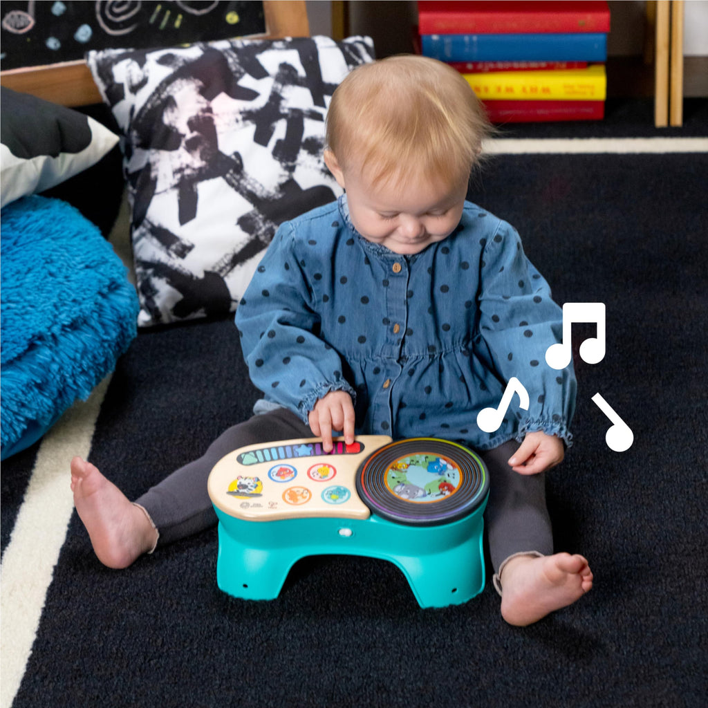 Blond toddler kneeling at teal discovery stool with wooden top and spinning picture dial