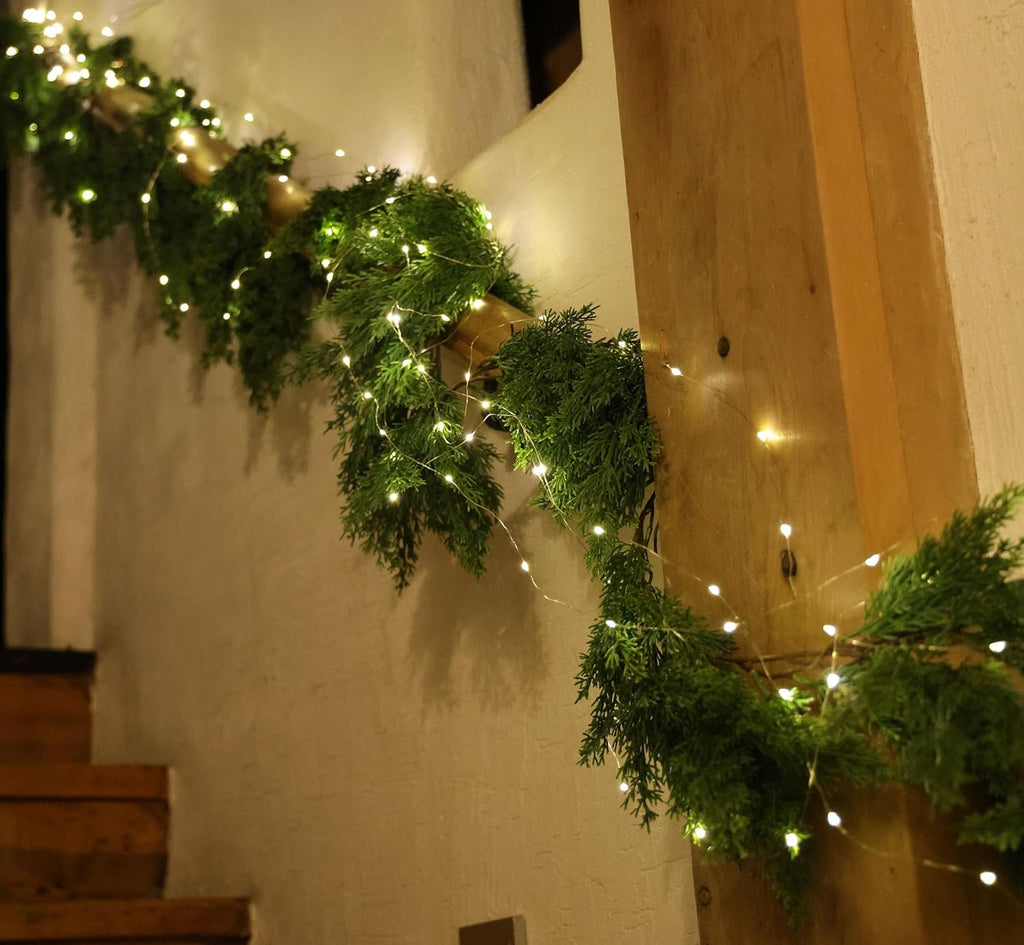 Artificial pine garland with warm LED lights along a wall corner, greenery strands in a row