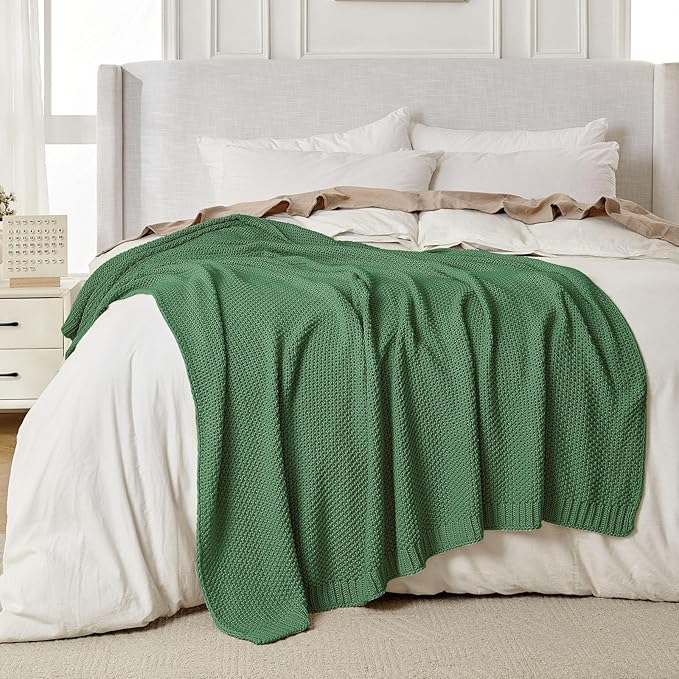 Chunky cable knit cotton throw blanket, olive green, spread across a bed