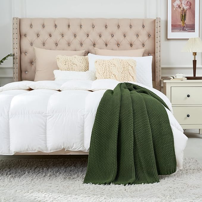 Olive green chunky knit throw blanket folded on a bed with white bedding