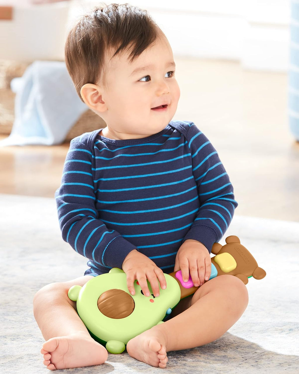 Baby seated holding green avocado guitar toy with brown tuning knobs
