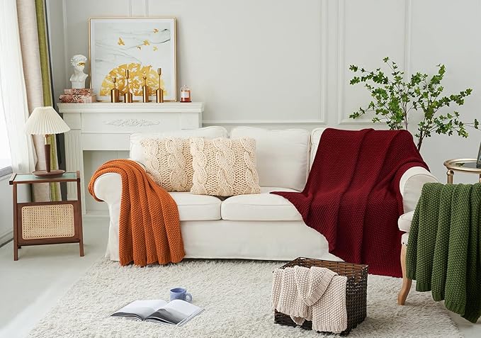 Wine red chunky cable-knit cotton throw blanket folded on a sofa with knit texture.