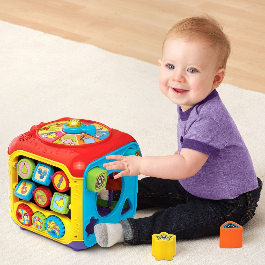 Red baby activity cube on floor with shape-sorting blocks