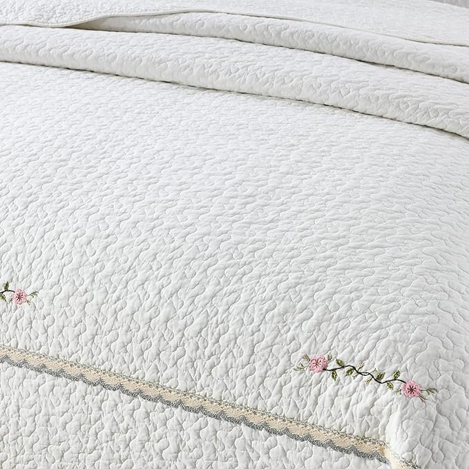Close-up of white quilt coverlet with textured quilting and floral embroidered edge trim