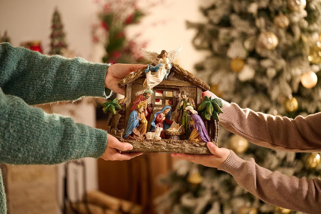Hands holding LED-lit resin nativity scene figurines with angel topper and manger