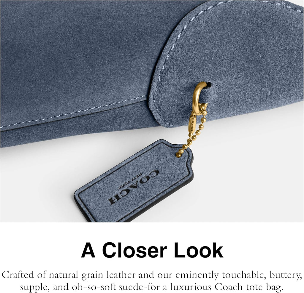 Navy suede bag close-up with contrast stitching and gold chain key fob.