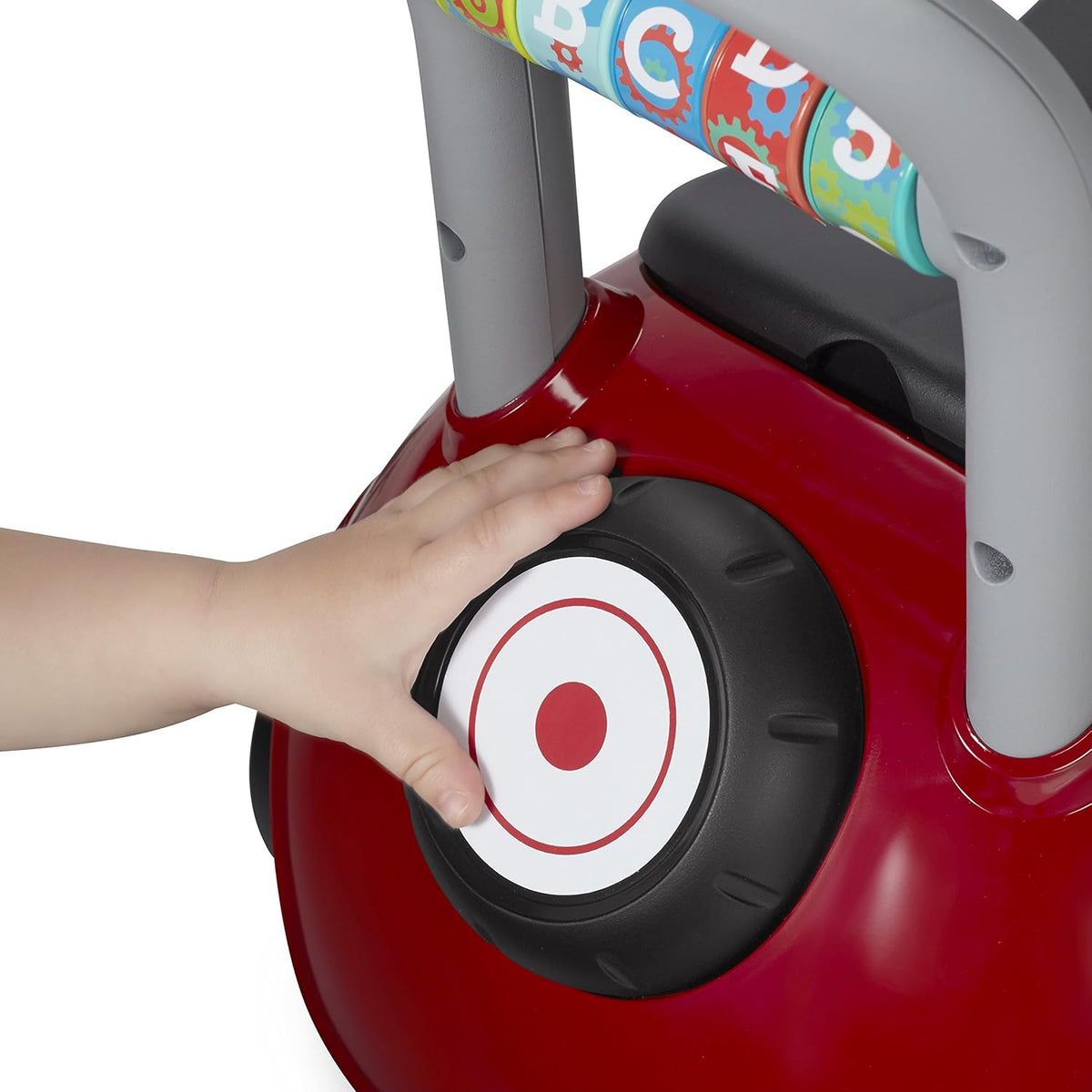Red toddler ride-on car wheel and round horn button on side of grey handle frame.