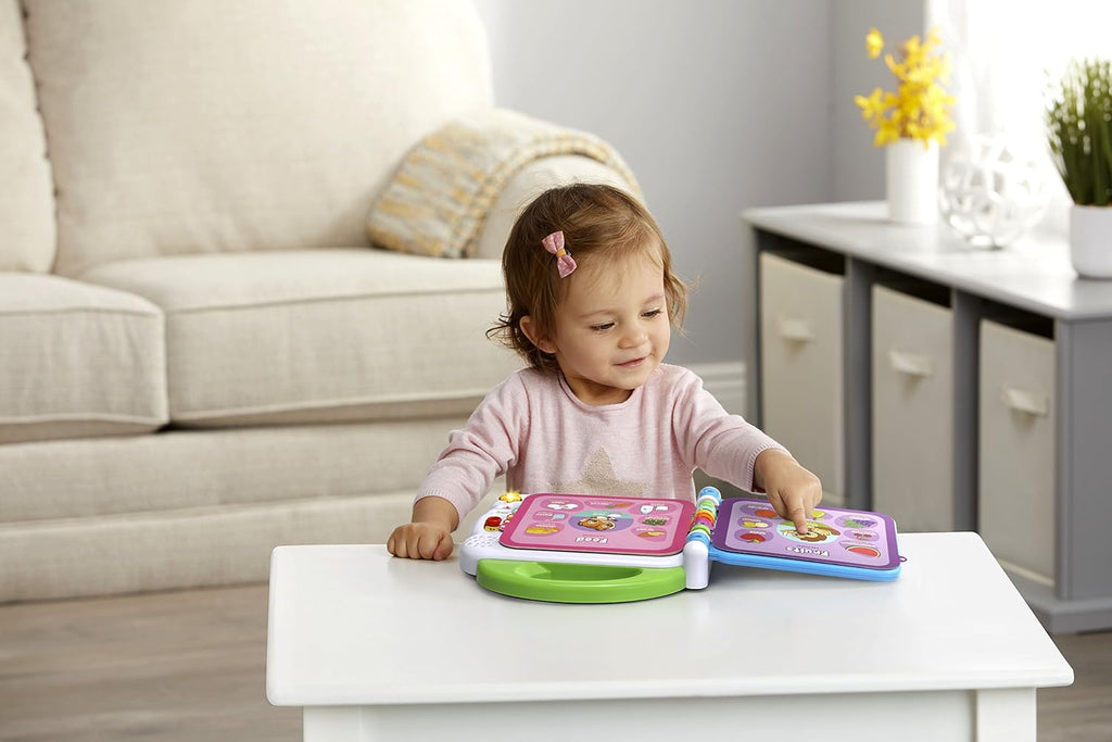 Young child playing with a green 100 words learning book toy on a table