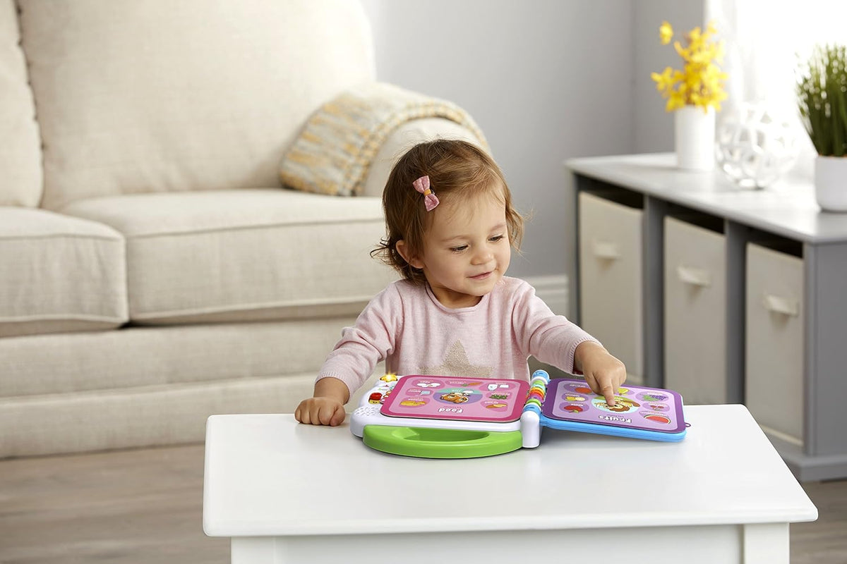 Young child playing with a green 100 words learning book toy on a table