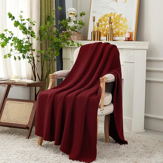 Wine red chunky cable-knit cotton throw blanket draped across a chair and floor.