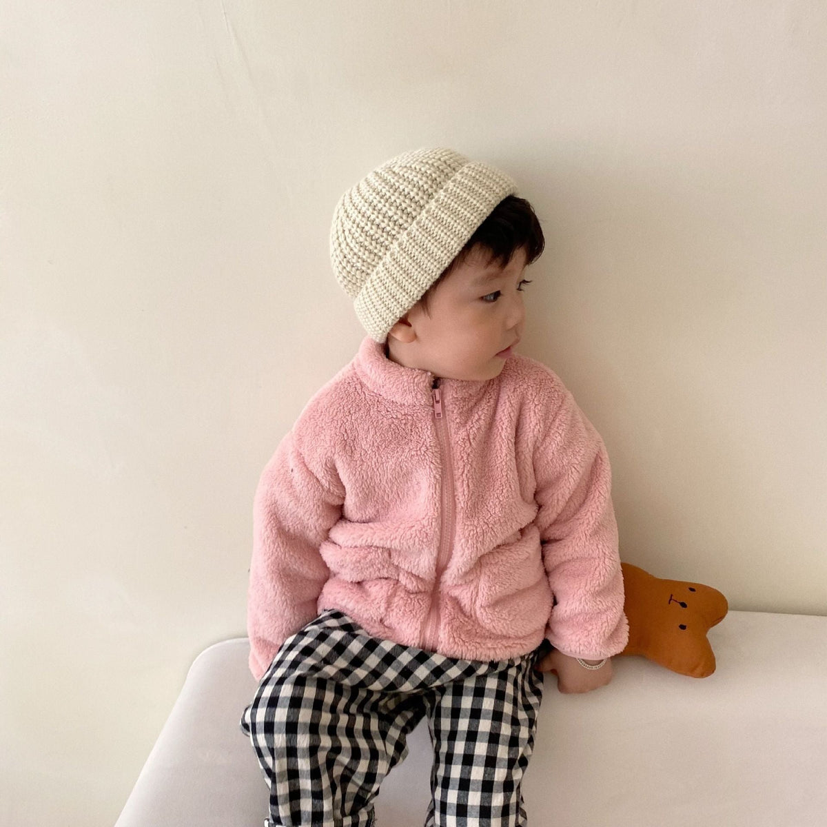 Pink kids fleece zip jacket with hood, worn with a cream knit beanie.