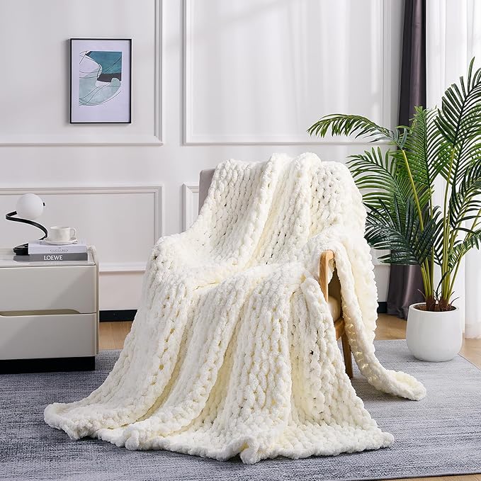 Cream chunky knit blanket throw with raised cable pattern, draped over sofa arm