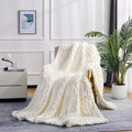 Cream chunky knit blanket throw with raised cable pattern, draped over sofa arm