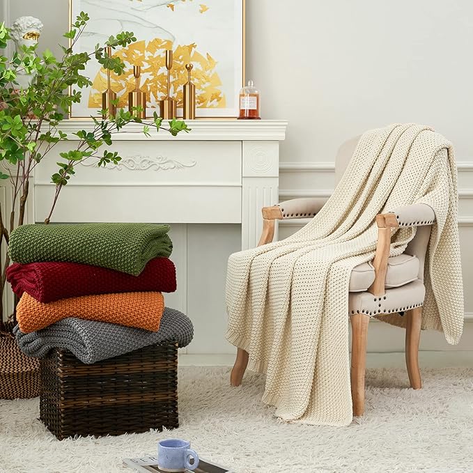 Wine red chunky cable-knit cotton throw blanket folded atop other blankets on the floor.