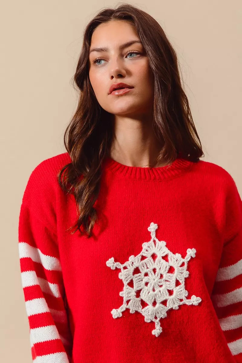 Red knit sweater close-up with white crochet snowflake applique and striped sleeve cuff