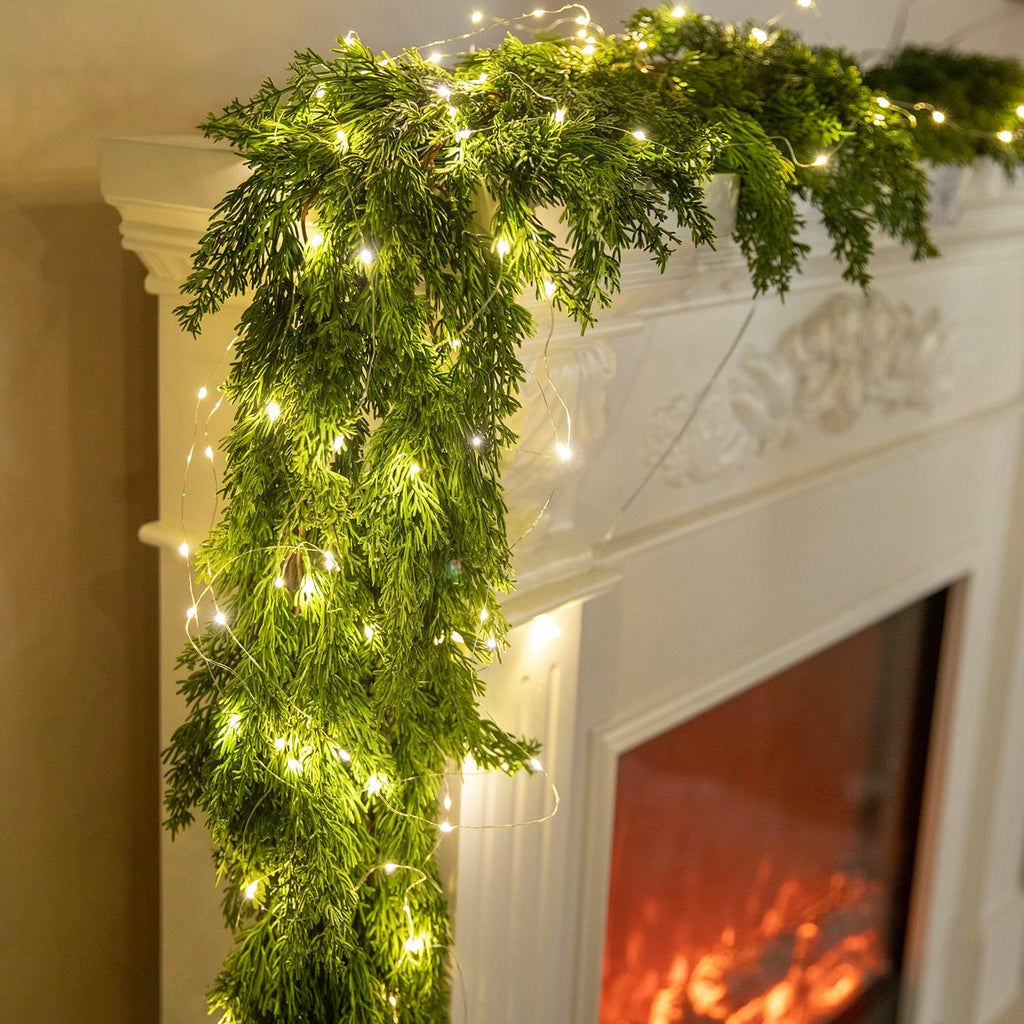 Artificial cypress-style garland with warm LED string lights hanging over a fireplace mantel