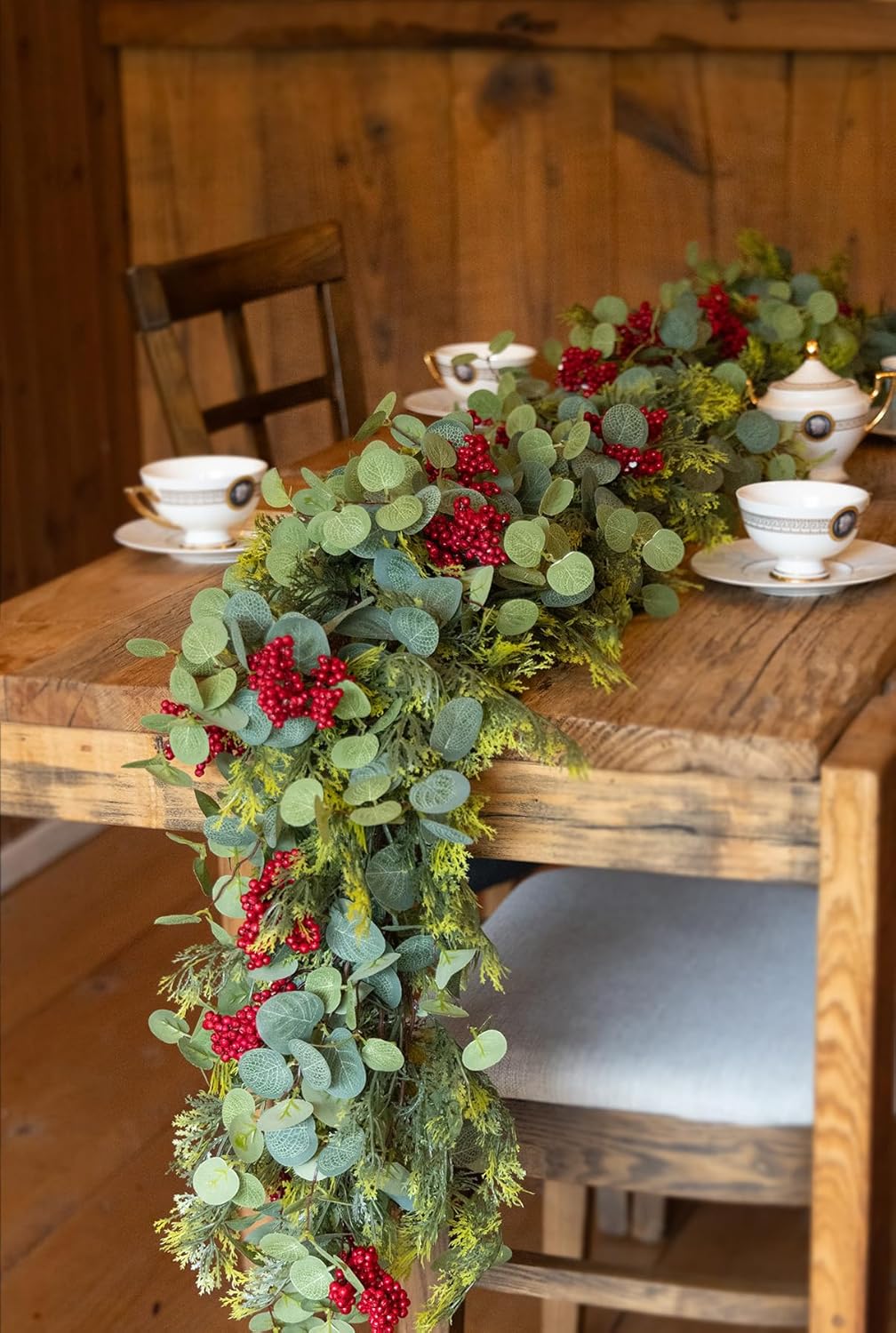 Artificial winter garland with green leaves, pine-cypress tips, and red berries on dining chair