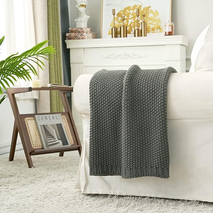 Chunky knit throw blanket in medium gray draped over a sofa arm.