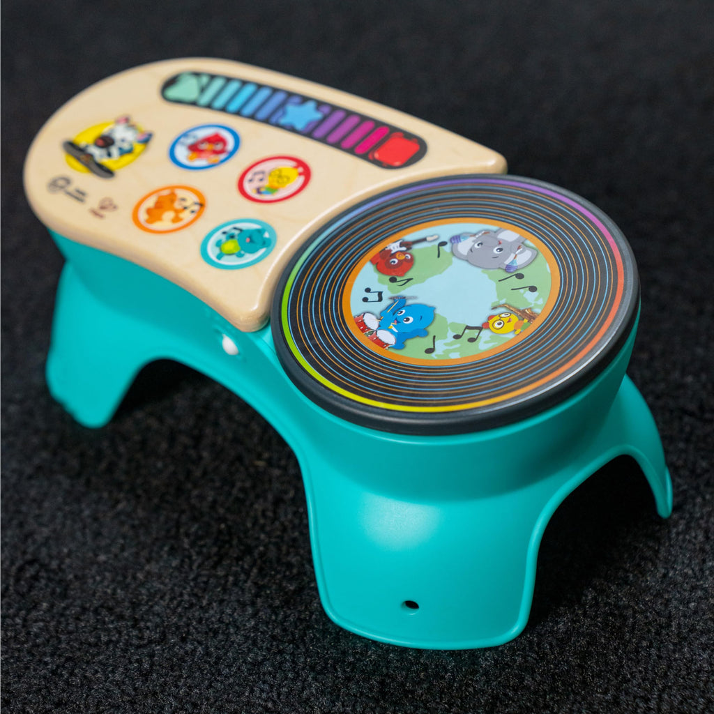 Teal toddler discovery stool in close-up: wooden top icons and round rotating drum