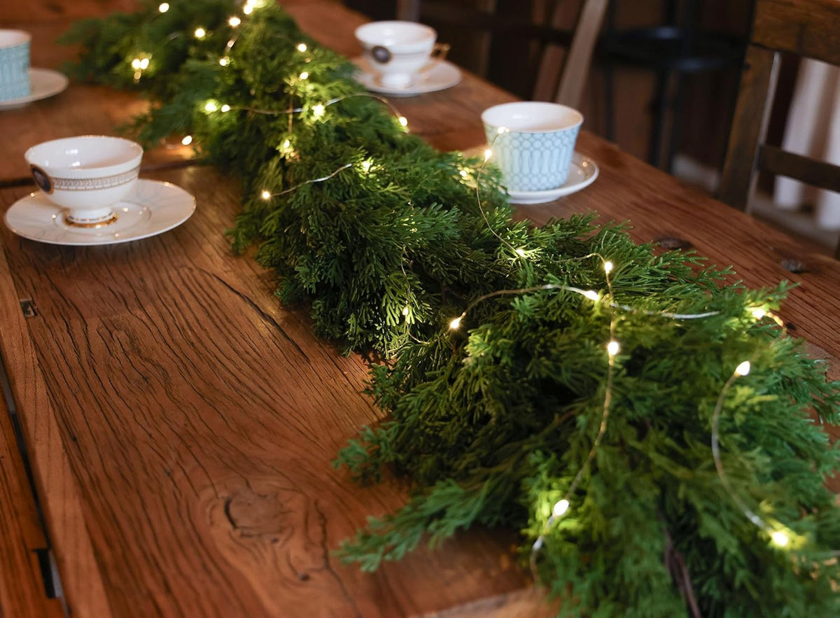 Artificial pine garland with warm LED lights laid across a wooden dining table surface