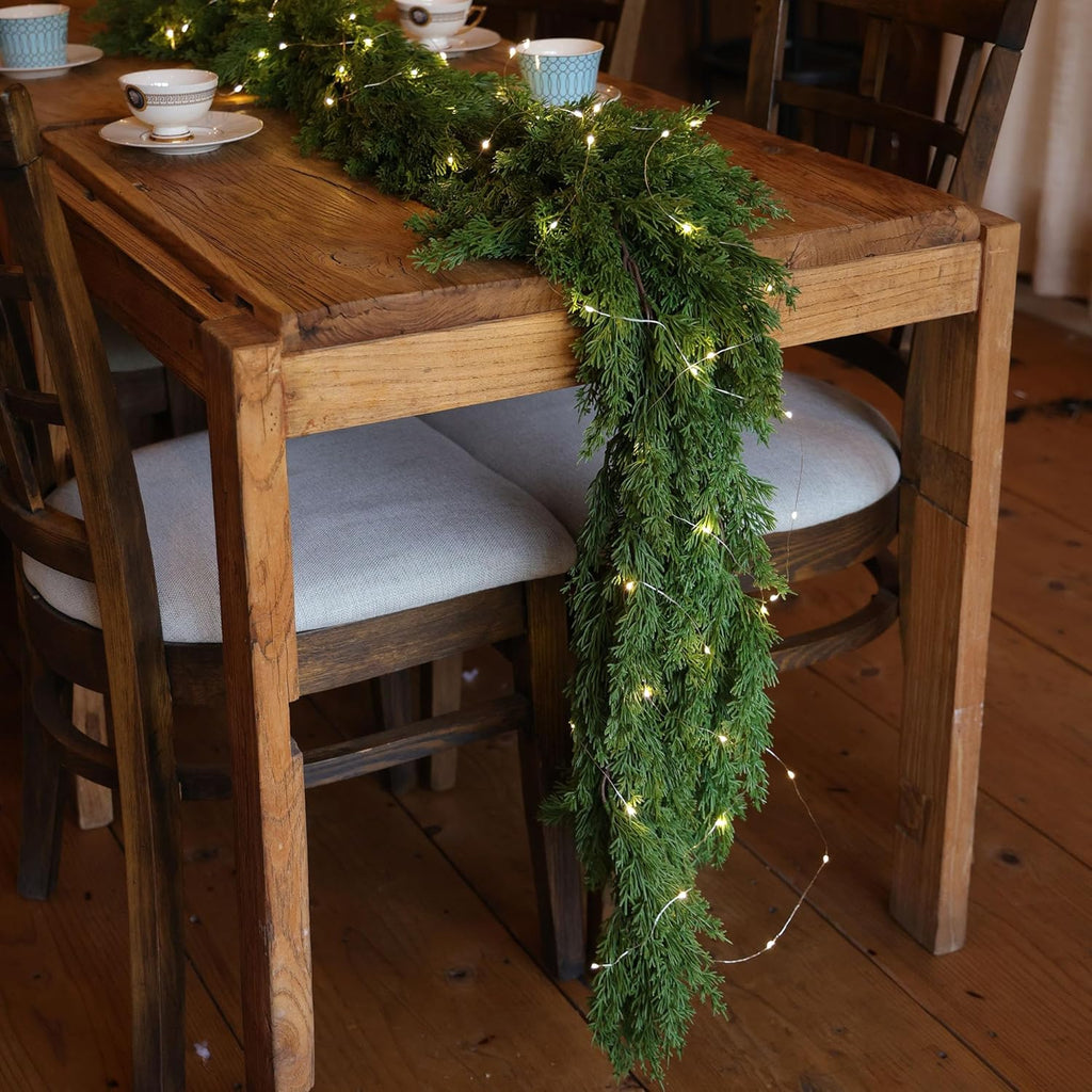 Artificial greenery garland with warm LED lights draped along a dining table chair back