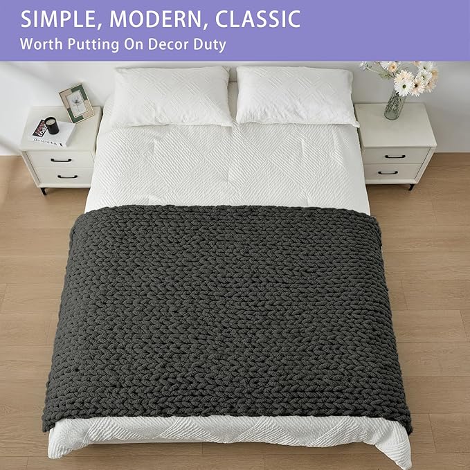 Dark grey chunky knit throw blanket folded on a bed, thick cable texture