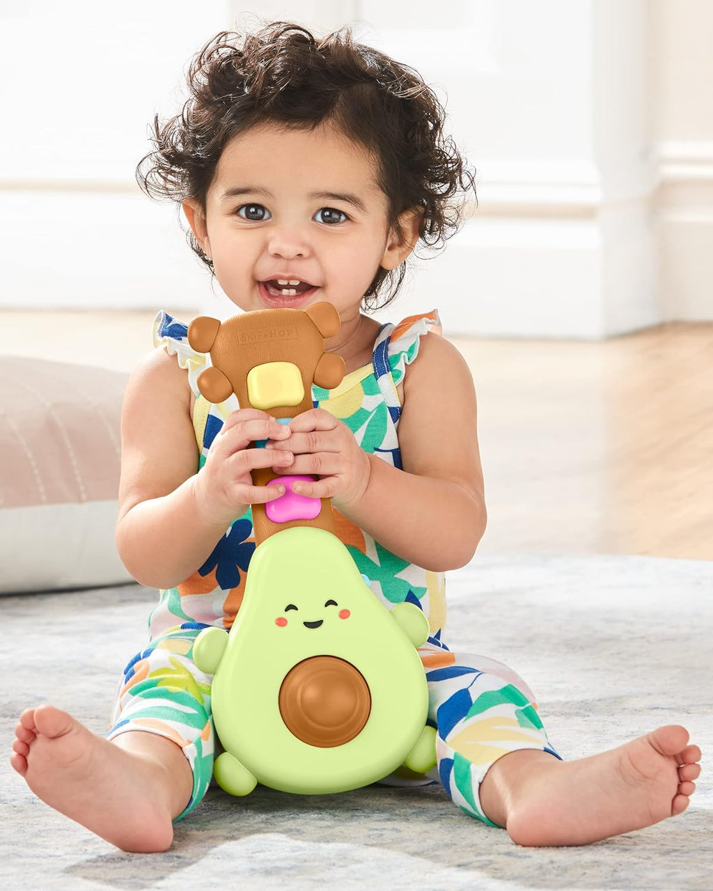 Baby holding green avocado guitar toy with orange and rainbow light-up buttons