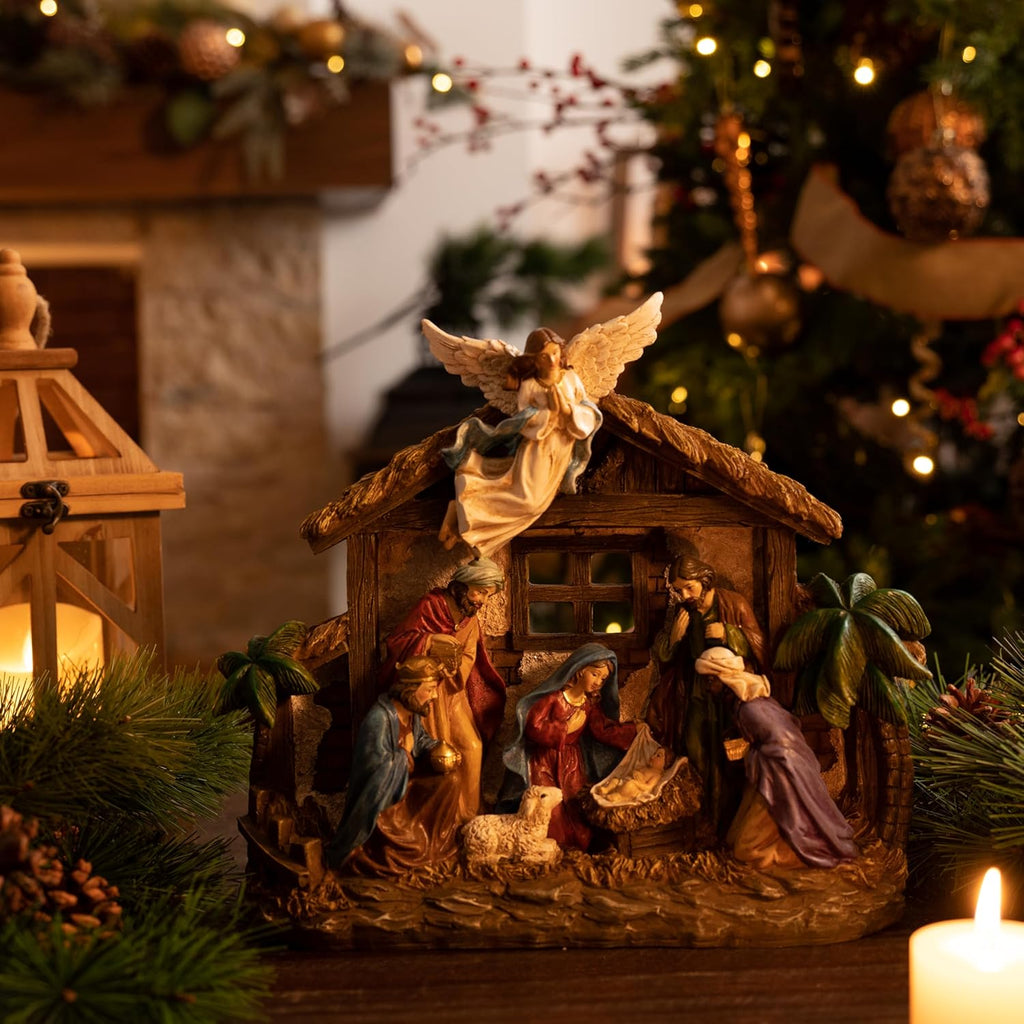 LED-lit nativity scene figurines in wooden stable with angel topper and candles nearby