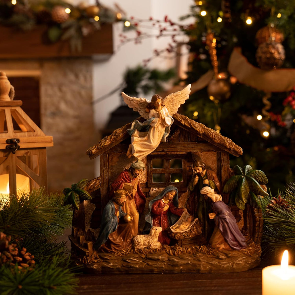 LED-lit nativity scene figurines in wooden stable with angel topper and candles nearby