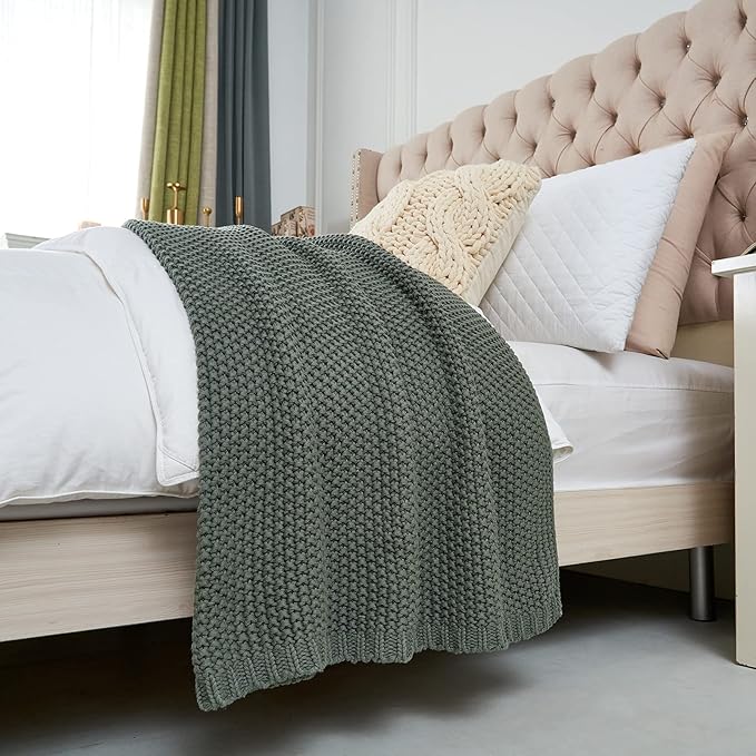 Chunky cable knit throw blanket in dark green draped over a sofa.
