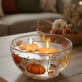Glass bowl candle with floating maple leaf-shaped wax candles and flames