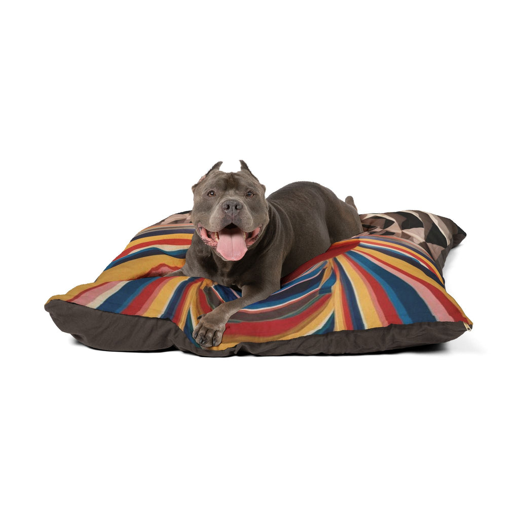 Plush pet bed with multicolor striped top and geometric accent; dog resting on it