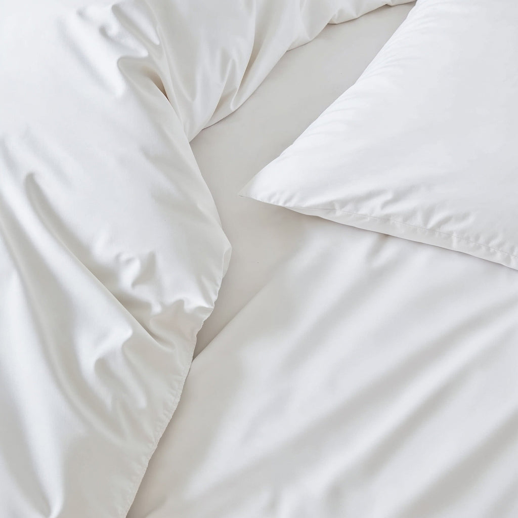 White sateen bedding bundle with folded flat sheet and duvet close-up