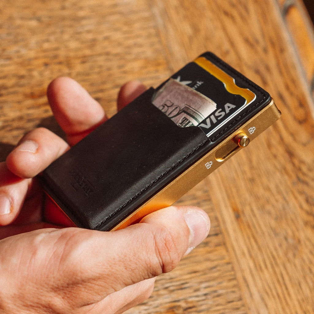 Black leather card wallet with gold-toned metal side detail and Visa card