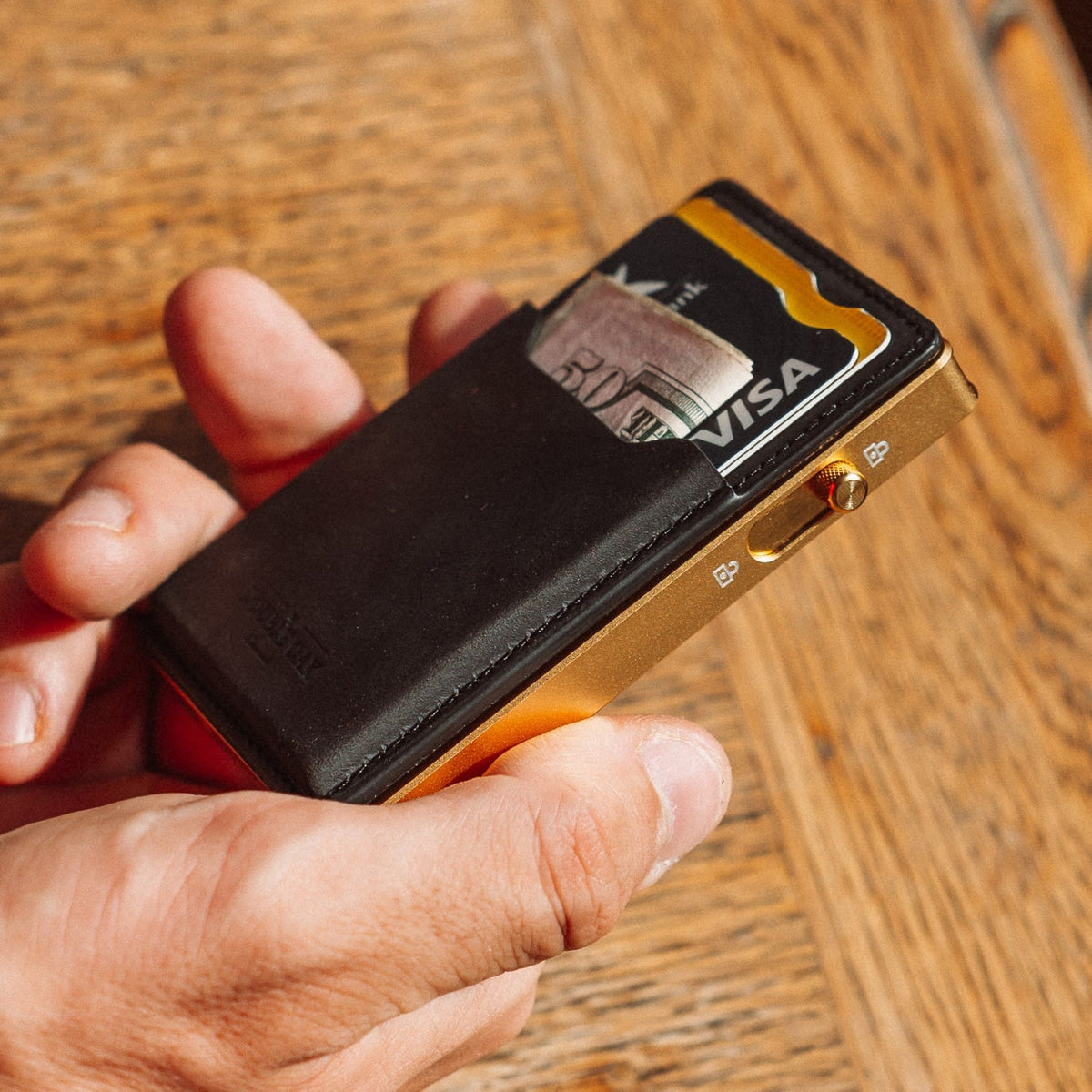 Black leather card wallet with gold-toned metal side detail and Visa card