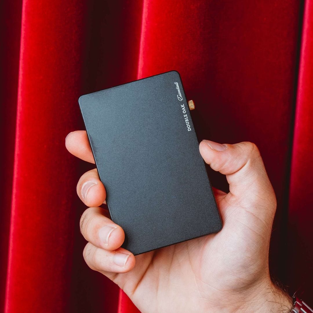 Charcoal pop-up cardholder held in hand, with brass button closure and label.