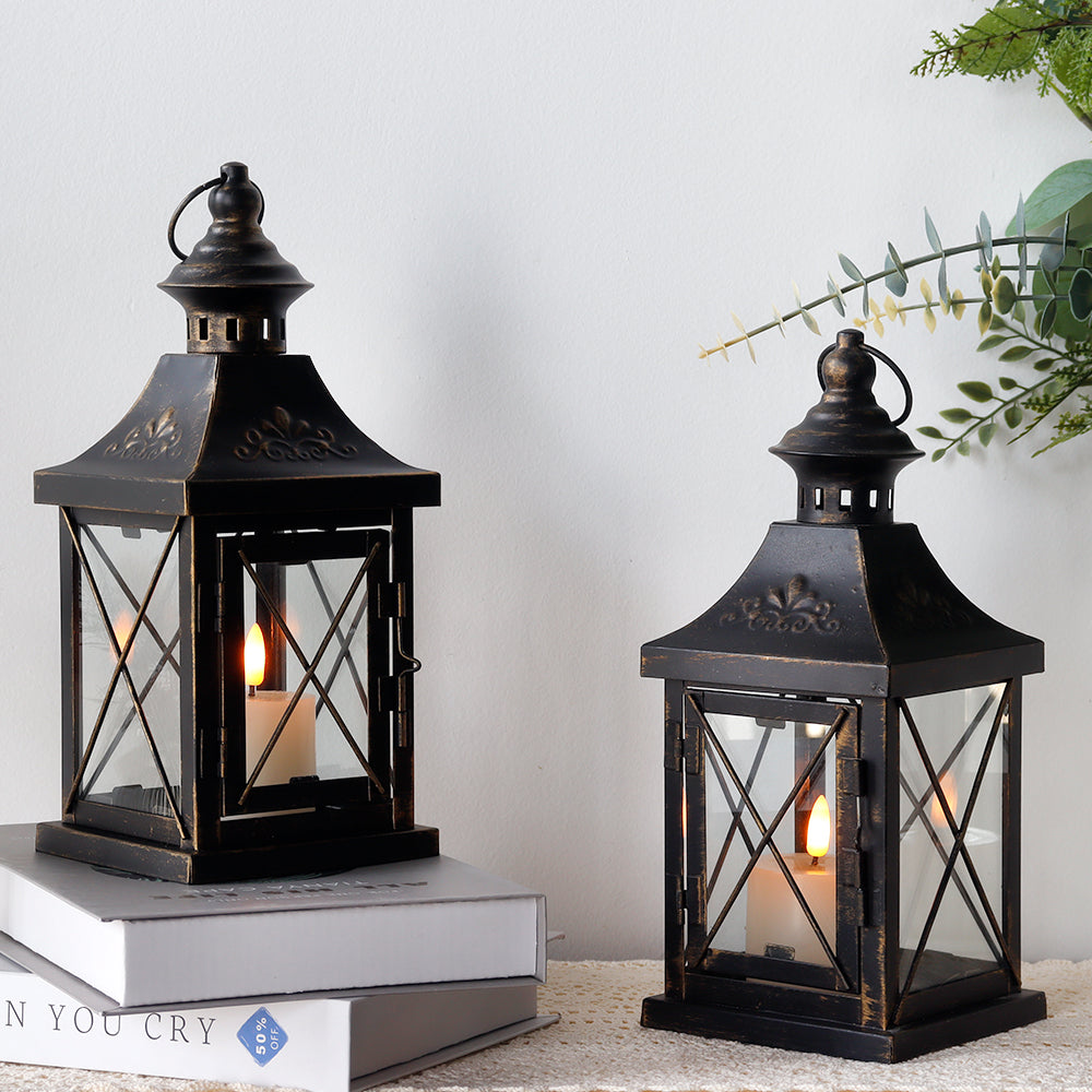 Two black metal candle lanterns with cross-brace glass sides and top loop handles
