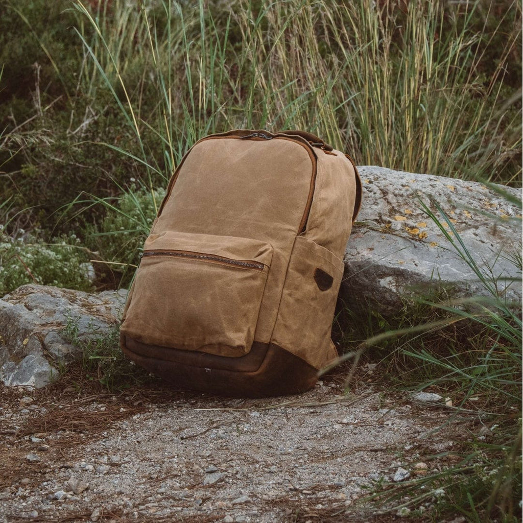 Sand waxed canvas backpack with leather-trim front pocket, standing on rocks
