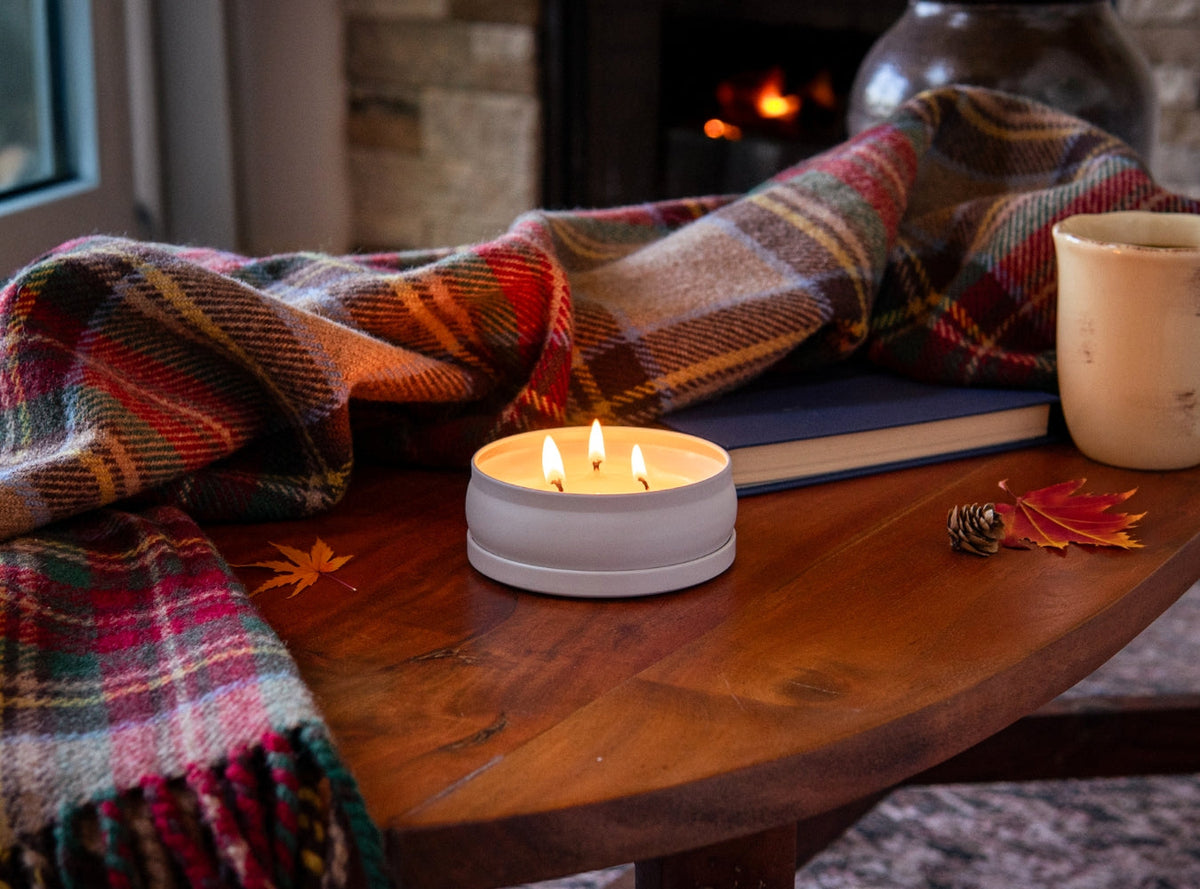 Lit 3-wick candle in a white round jar on a wooden surface