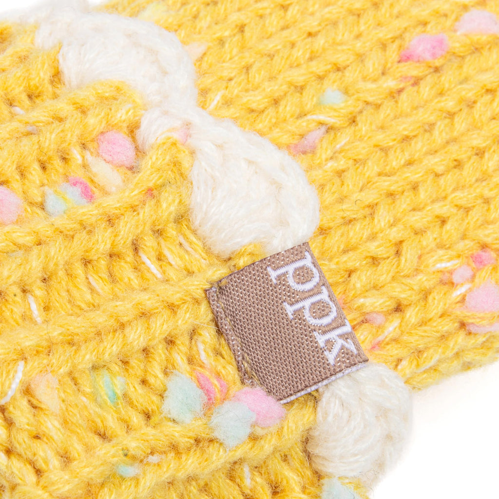 Close-up of yellow knit mitten with white cuff and brown leather brand label.