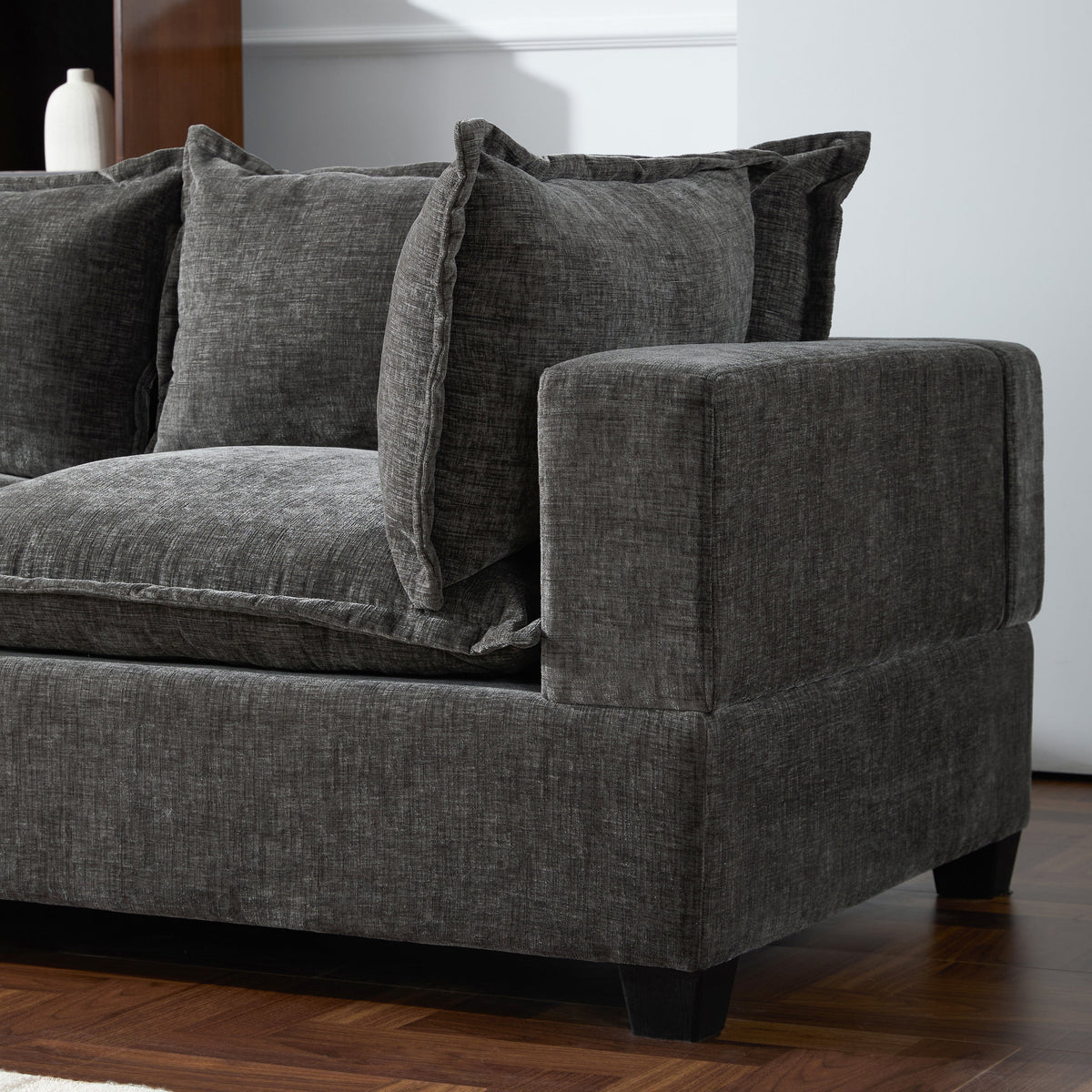 Gray chenille sectional sofa arm with stitched cushion and decorative pillows.