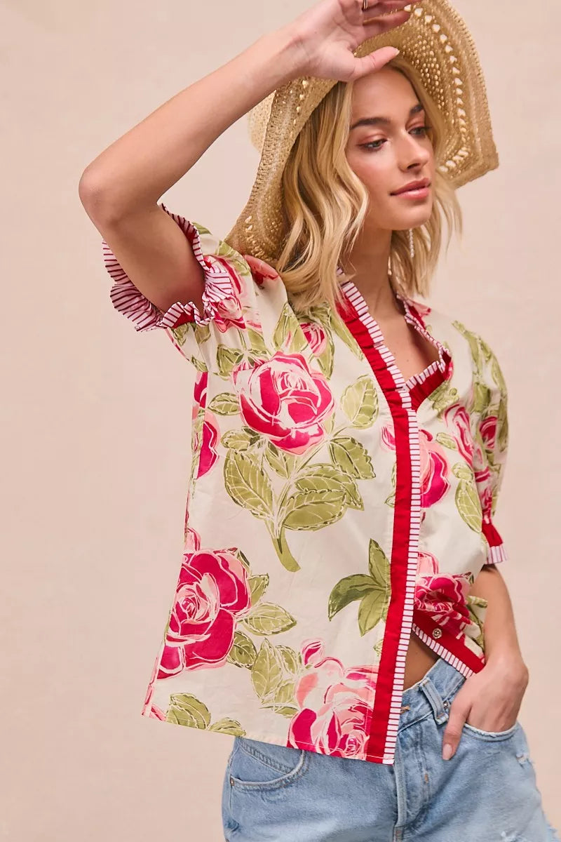 Floral blouse with coral vertical trim, V-style neckline, and ruffled sleeve cuffs