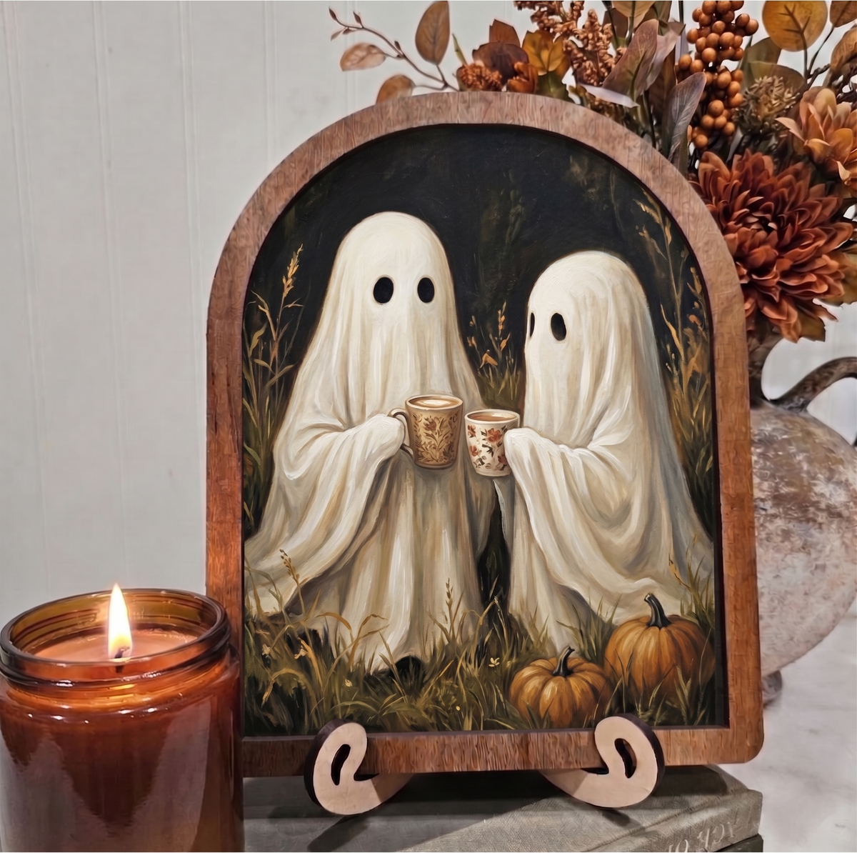 Arched framed Halloween art with two ghost figures holding coffee mugs, on wooden stand