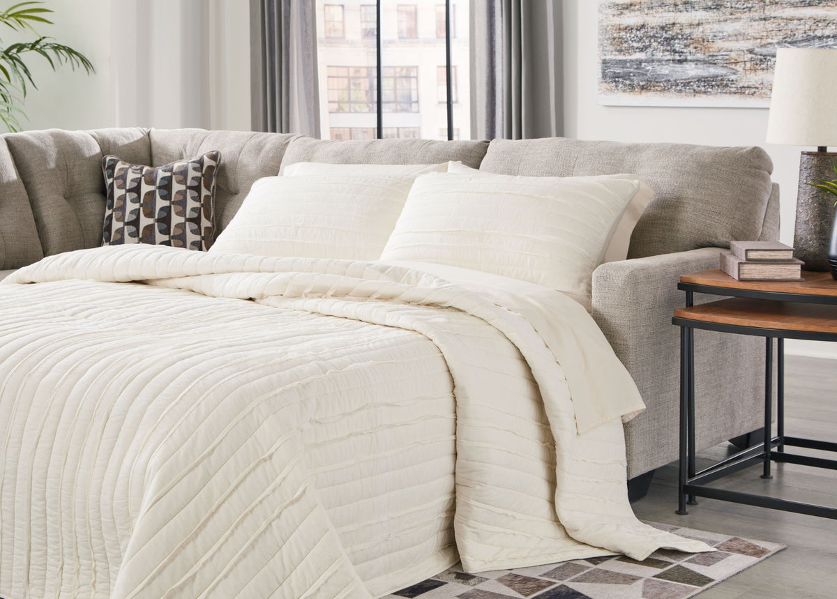 Light gray corner chaise sleeper sectional with pull-out mattress and layered bedding