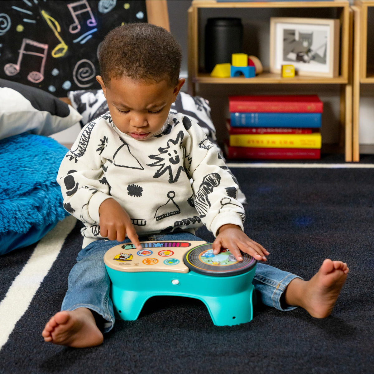 Toddler seated playing with teal discovery stool featuring wooden panel and rotating drum