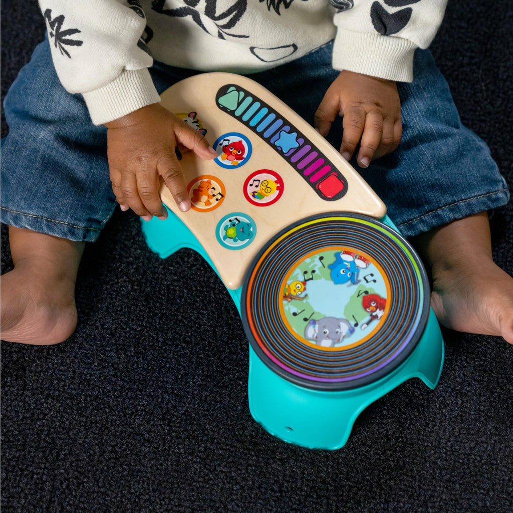 Teal and wood toddler discovery stool held by hands; rotating drum with animal graphics