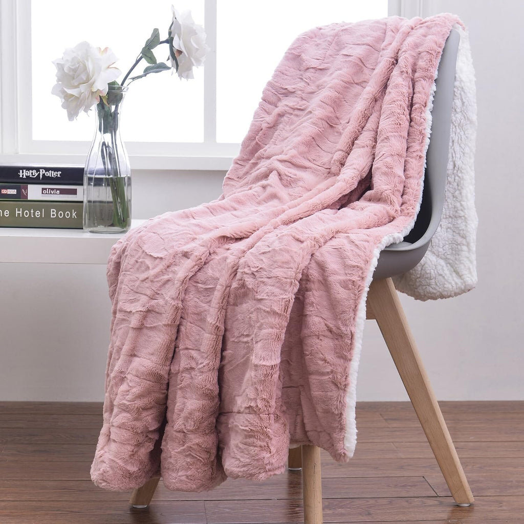 Dusty pink faux fur throw blanket with white sherpa-style reverse edge, draped
