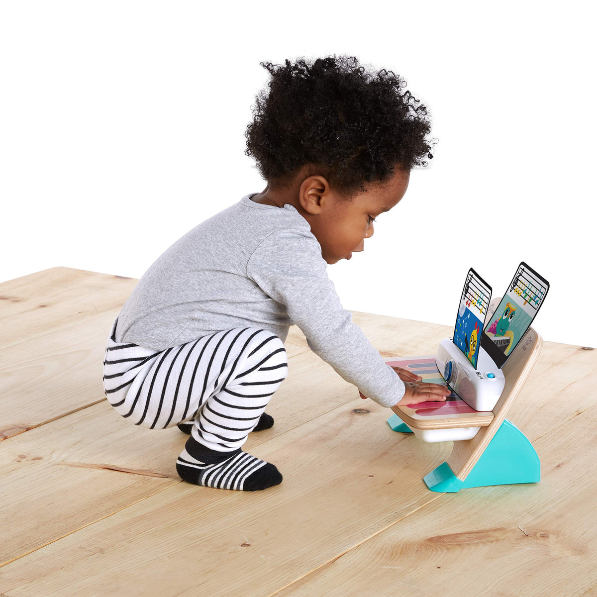 Toddler kneeling to play a wooden music piano with lit tablet screen